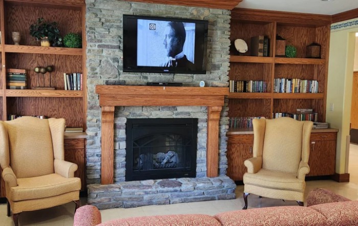 A cozy living room featuring a stone fireplace with a television mounted above, flanked by bookshelves and armchairs.