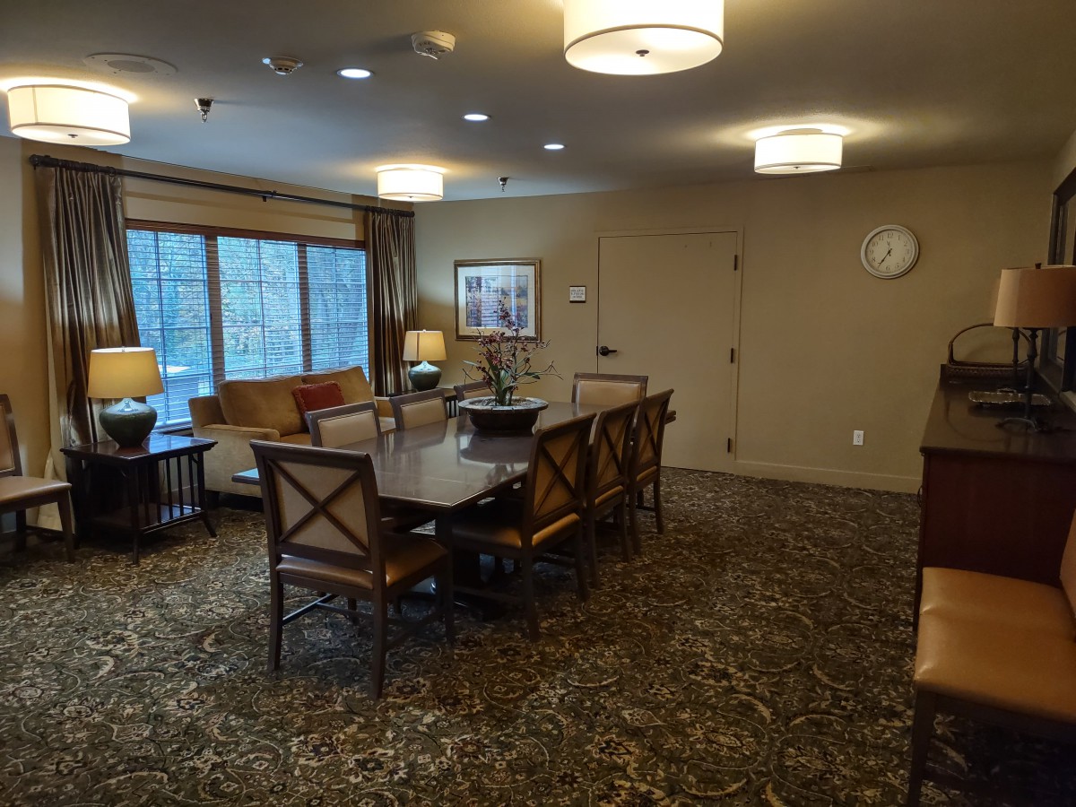 A cozy conference room with a large table surrounded by chairs, featuring warm lighting and a window view.