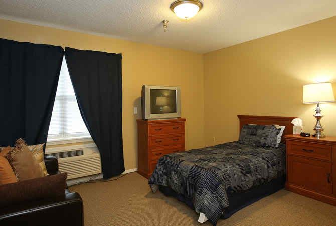 A cozy bedroom with a single bed, a television on a dresser, and dark curtains on the window.