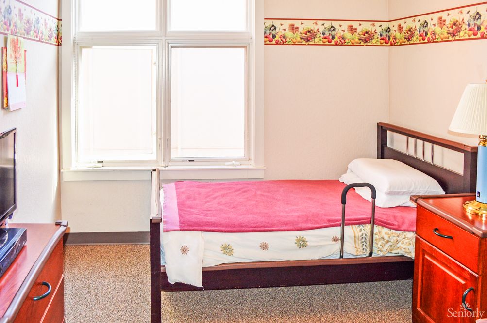 A minimalist bedroom with a single hospital-style bed near a window.