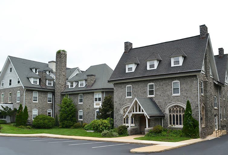 A large stone building with gabled roofs and multiple windows, surrounded by greenery.