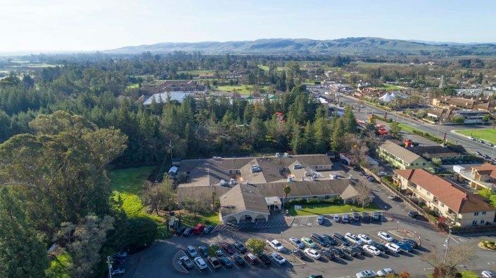 Aerial view of a building complex surrounded by trees and a parking lot, set in a suburban landscape.
