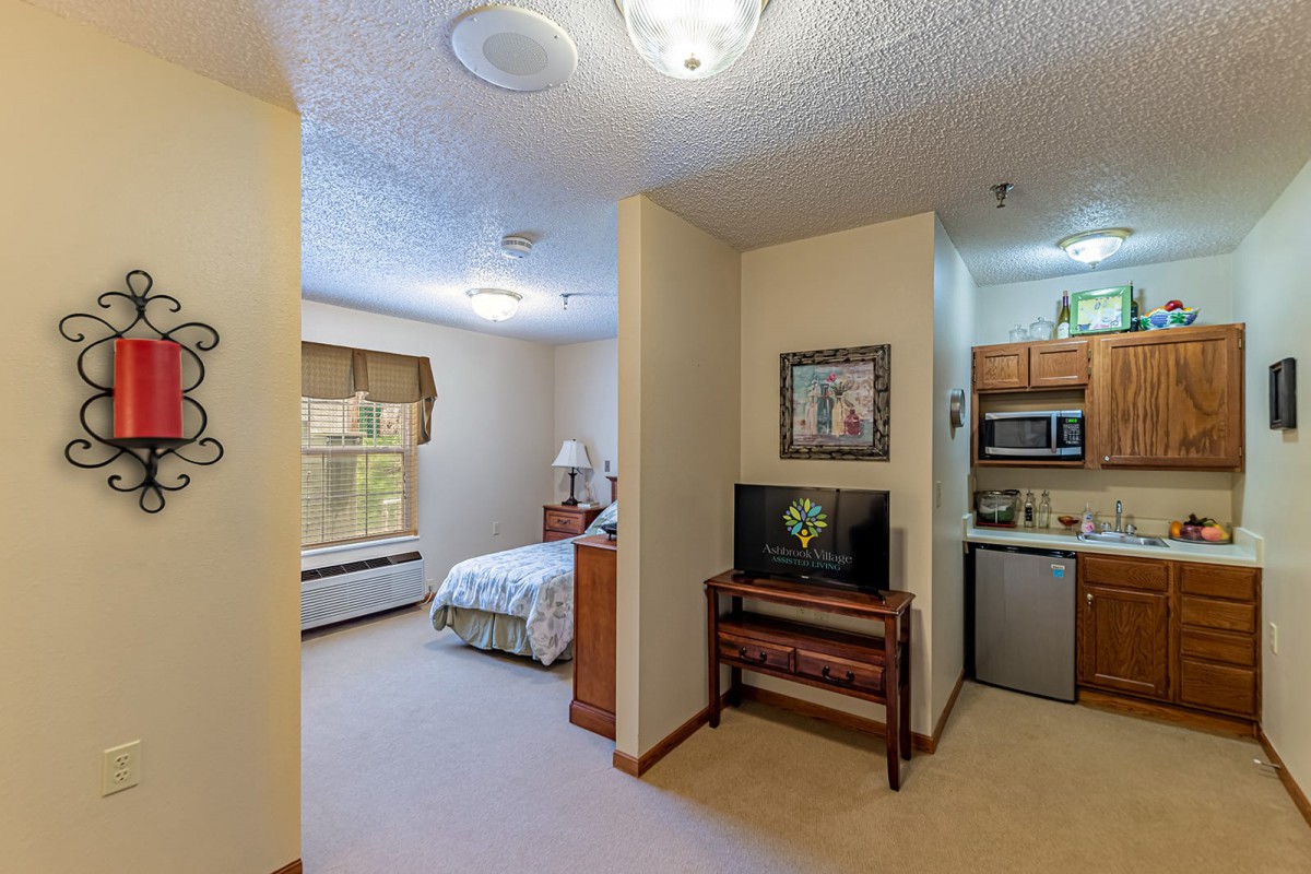A compact apartment with a cozy bedroom and kitchenette, featuring modern furniture and decor.