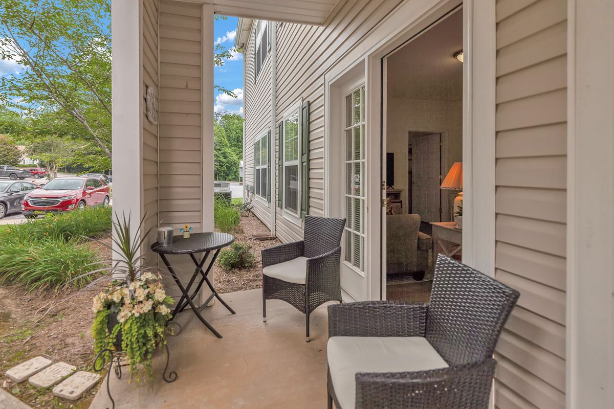 A cozy outdoor patio area featuring wicker chairs, a small round table, and potted plants.