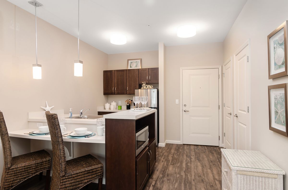 A modern kitchen with a bar counter and wood flooring, featuring dark cabinets and pendant lighting.