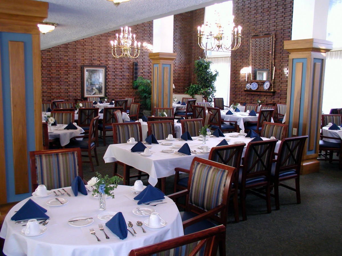An elegant dining room with neatly arranged tables and chairs, featuring white tablecloths and blue napkins.