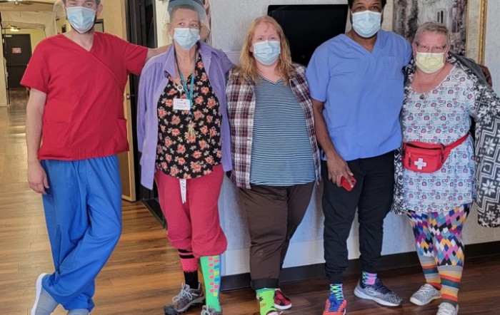 A group of healthcare workers wearing masks and colorful socks, standing together indoors.