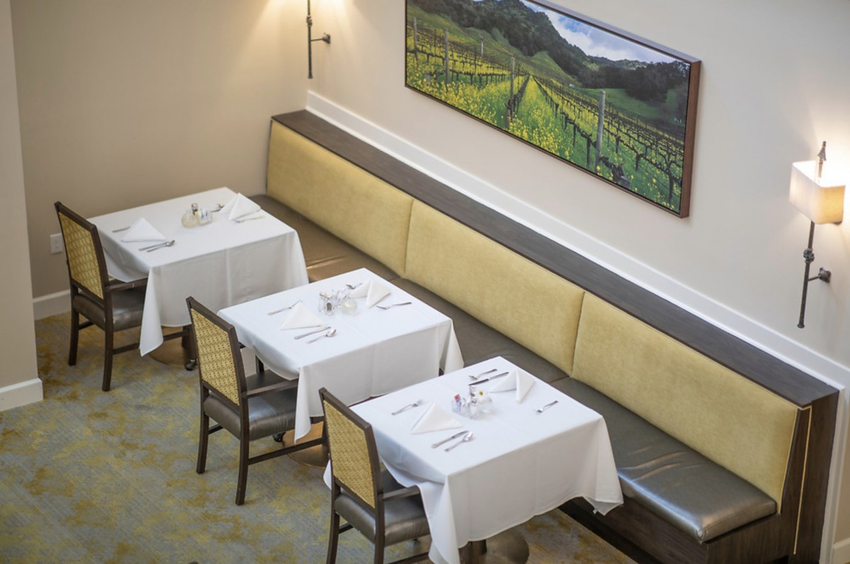 An empty restaurant dining area with neatly set tables and a landscape painting on the wall.