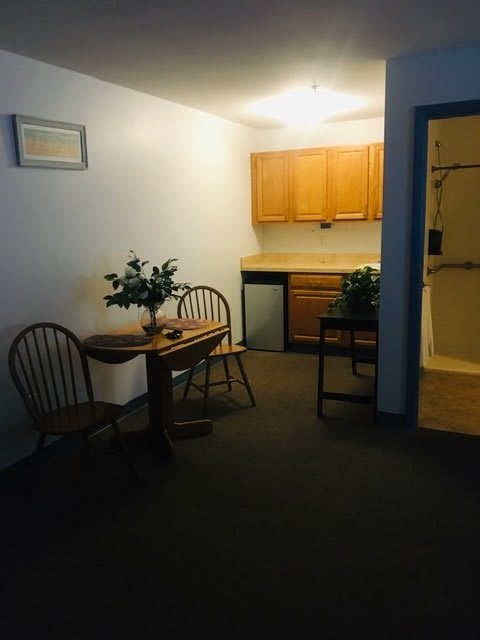 A cozy kitchen and dining area with wooden cabinets, a small table, and chairs. Two potted plants add a touch of greenery to the space.