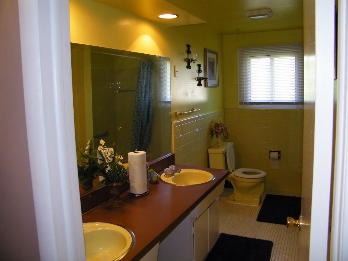 A bathroom with yellow walls featuring a double sink, a mirror, and a window.