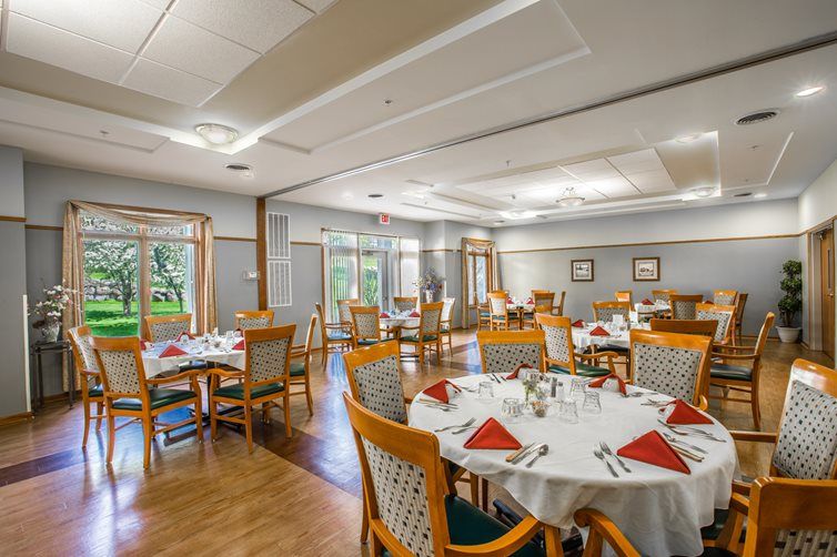 An elegantly set dining room with round tables and wooden chairs, featuring neatly arranged table settings.