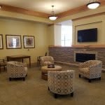 A cozy living room with armchairs arranged around a central table, featuring a fireplace and a wall-mounted television.