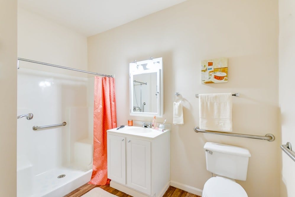 A bright bathroom with a shower, sink, and mirror featuring orange accents.