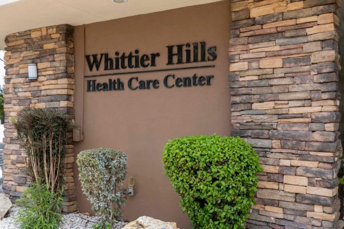 Entrance sign of Whittier Hills Health Care Center surrounded by landscaping.