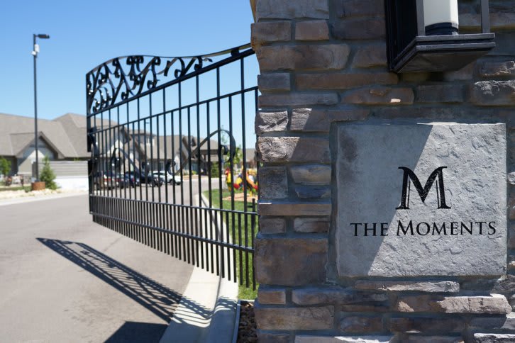 Entrance to a gated community with an ornamental iron gate and stone wall.
