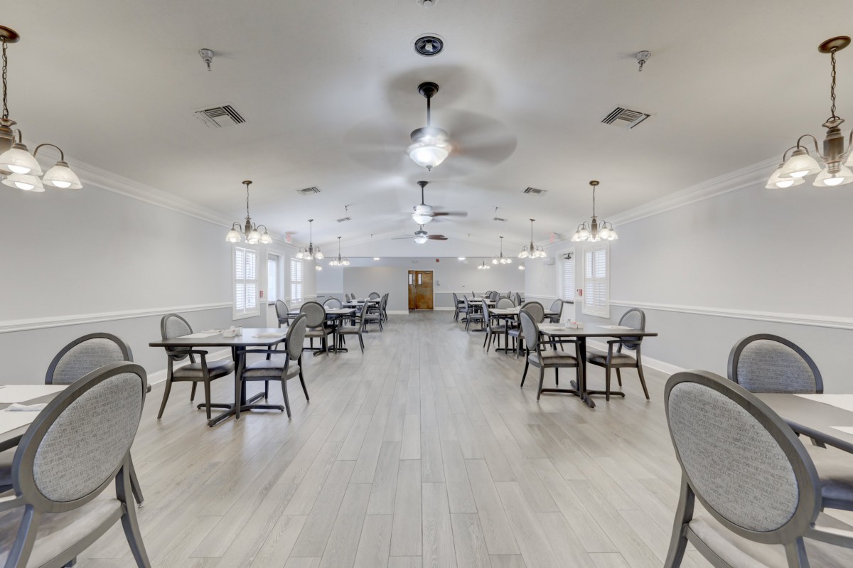 A spacious dining area with multiple tables and chairs, featuring bright lighting and ceiling fans.