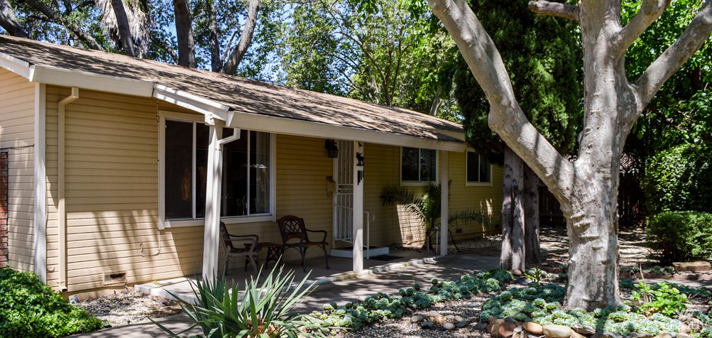 A small house with a porch surrounded by trees and a garden.