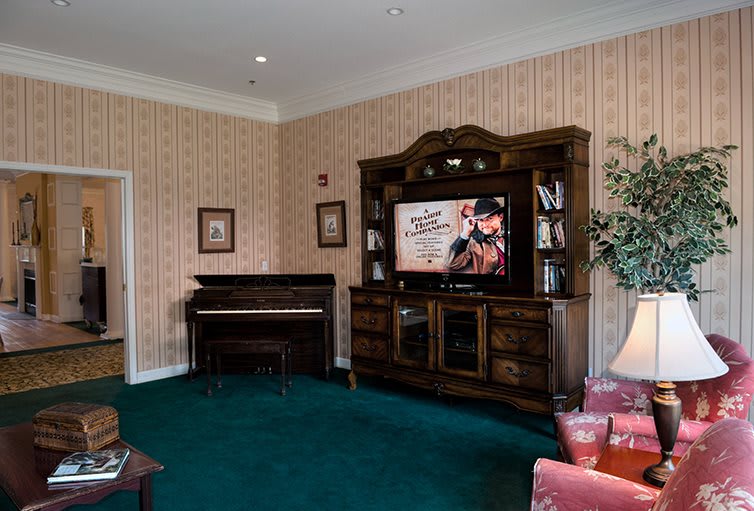 A cozy living room with a piano and an entertainment center featuring a large television.
