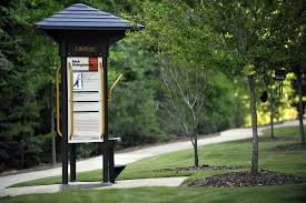 An information board stands next to a pathway in a lush, green park.