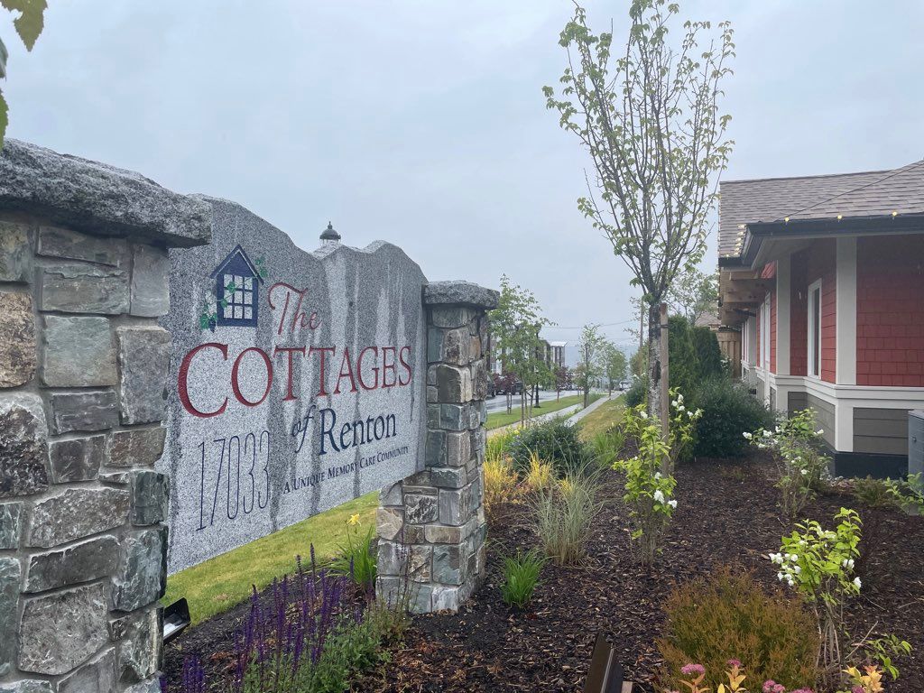 A stone sign for 'Cottages' with well-maintained landscaping and trees on an overcast day.