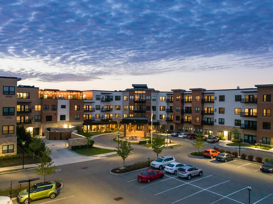 A modern apartment complex with a parking lot under a picturesque evening sky.