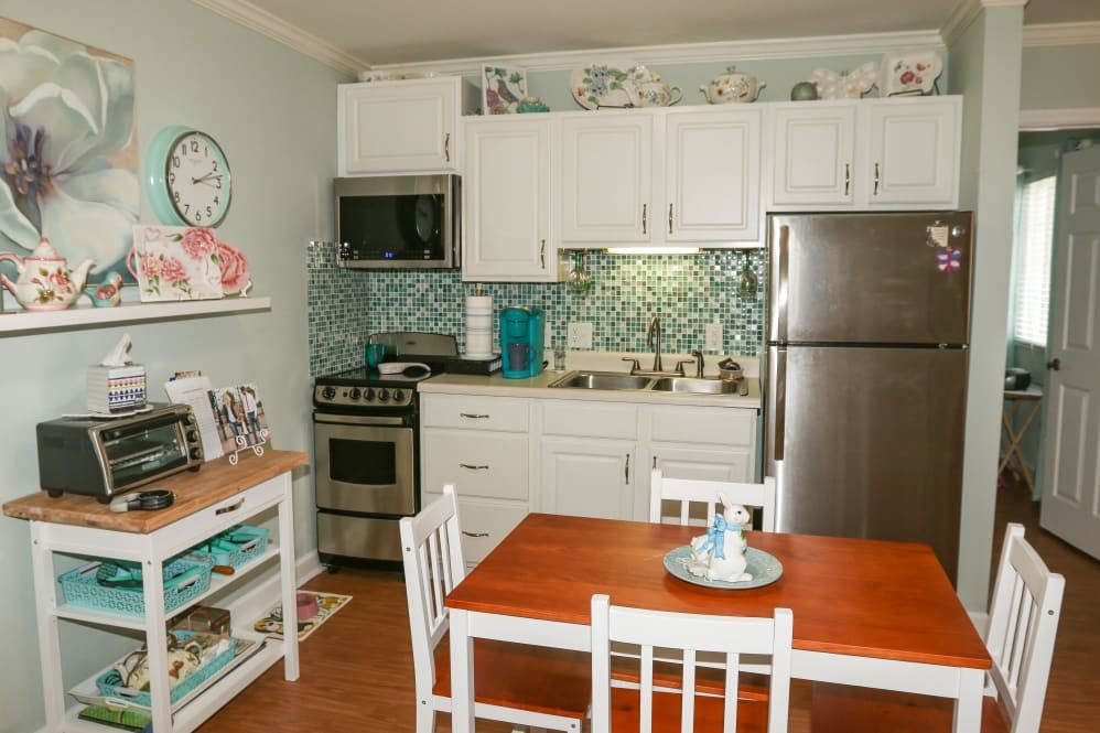 A modern kitchen and dining area featuring white cabinets, stainless steel appliances, a wooden table with chairs, and stylish decor.