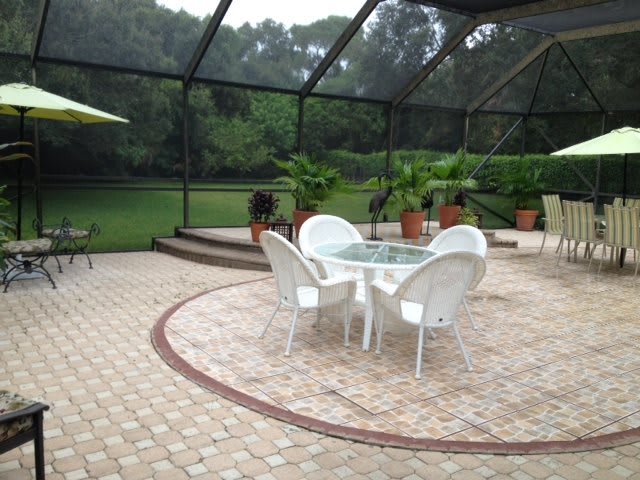 A screened-in patio area with a glass table surrounded by white chairs, featuring potted plants and a view of the garden.