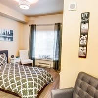 A cozy bedroom with a patterned bedspread, a chair by the window, and wall decorations.
