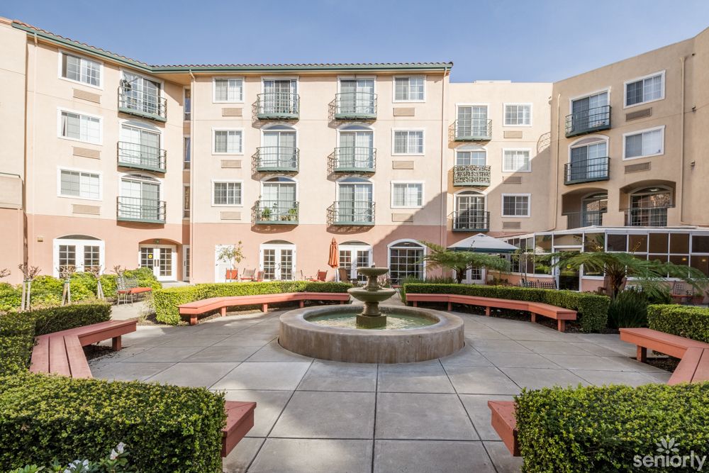 A sunny courtyard with a central fountain surrounded by benches and a modern apartment building.