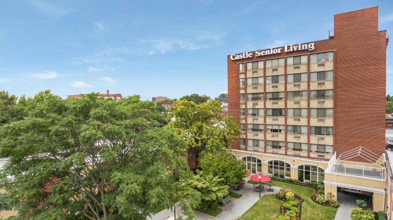 A hotel building surrounded by greenery under a clear blue sky.