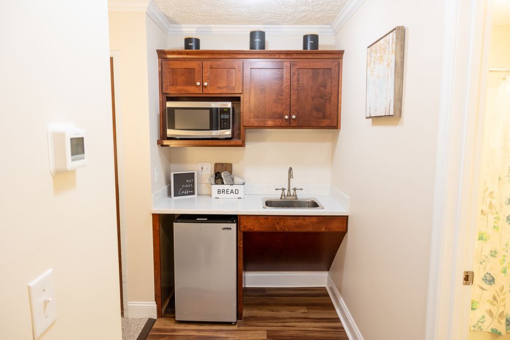 A compact kitchenette featuring a microwave, a mini refrigerator, and a small sink with overhead cabinets.