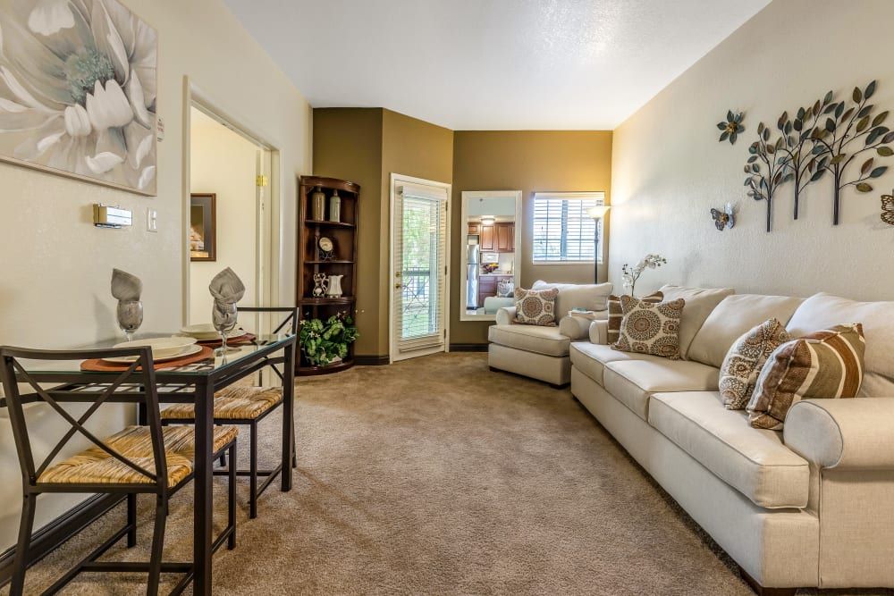 A cozy living room with a beige sofa, carpeted flooring, and a large mirror on the wall.