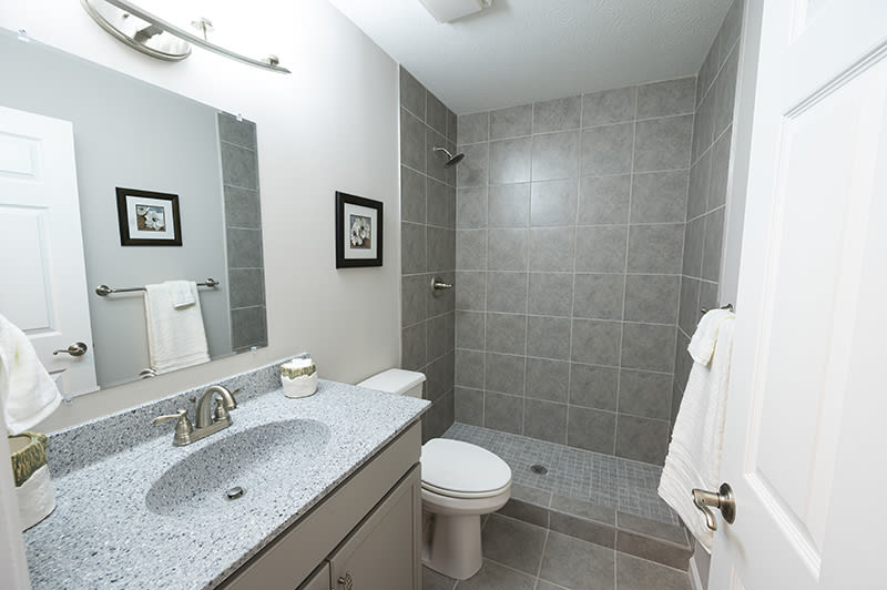 A modern bathroom featuring a walk-in shower, sink, and toilet with gray tiles.