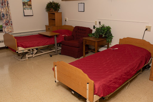 A simple hospital room featuring two beds, a reclining chair, and a small table.