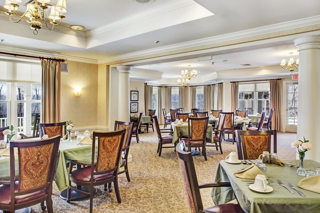 An elegant dining room with neatly arranged tables and chairs, featuring chandeliers and warm lighting.