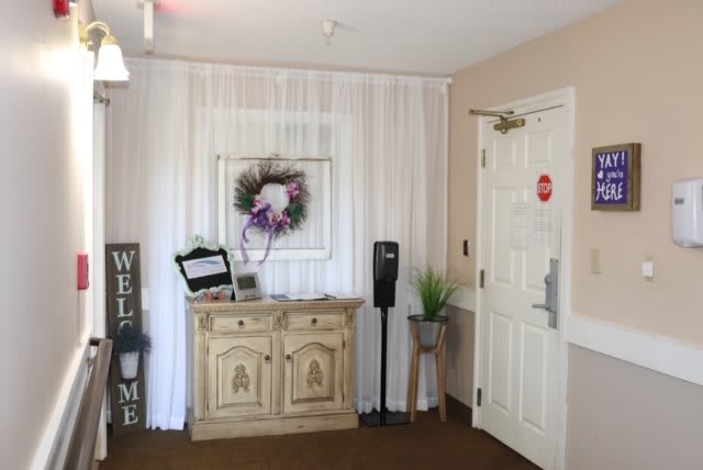 A cozy entrance area with a wooden cabinet, welcome sign, floral decor, and a door.