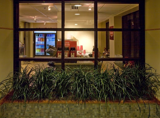 A nighttime view of a cozy lobby area through a glass window, showcasing modern furniture and greenery.