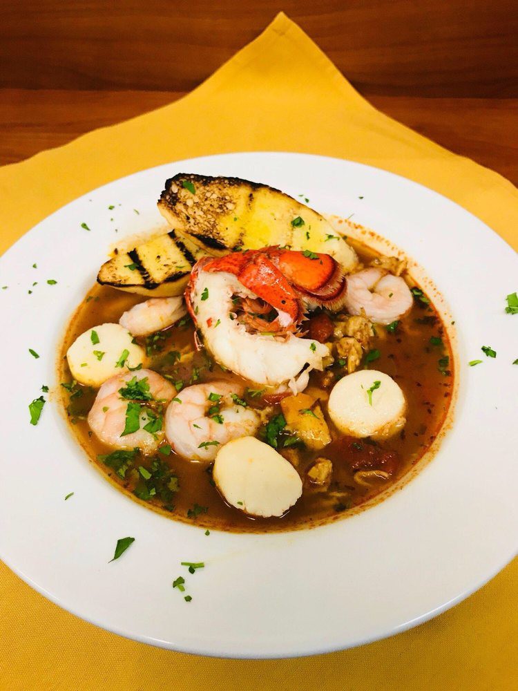A gourmet seafood soup with shrimp, scallops, and grilled pineapple, garnished with herbs.