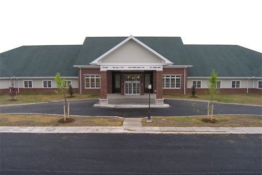 A brick library building with a green roof and main entrance flanked by small trees.