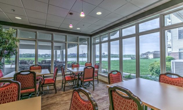 A dining area with tables and chairs, featuring large windows offering a scenic view.