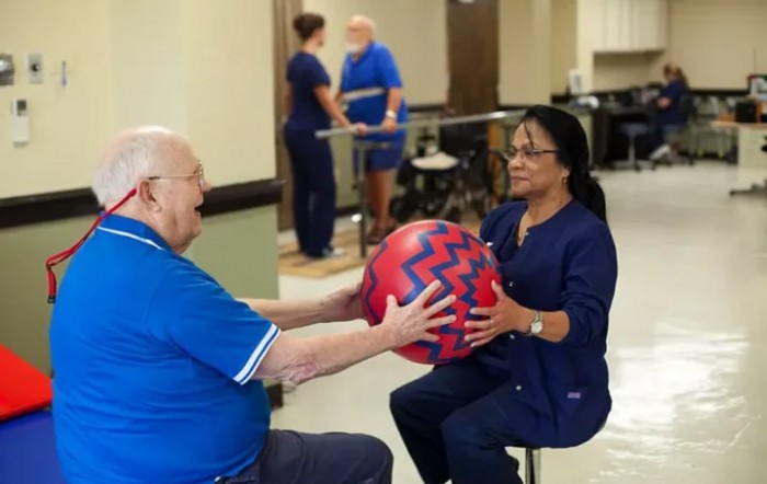 A healthcare professional assists a patient with an exercise routine using a large ball during a physical therapy session.