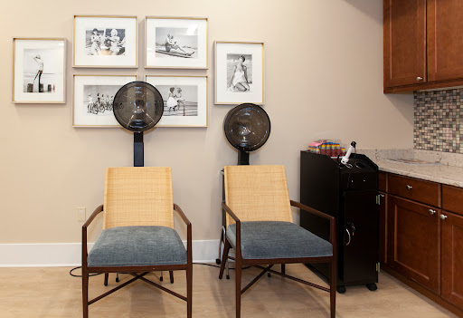 A cozy corner featuring two stylish chairs, framed artwork on the walls, and standing fans for comfort.