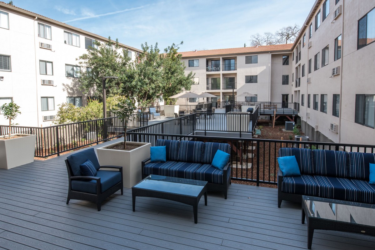 A modern outdoor seating area in an apartment complex with a view of surrounding buildings and trees.