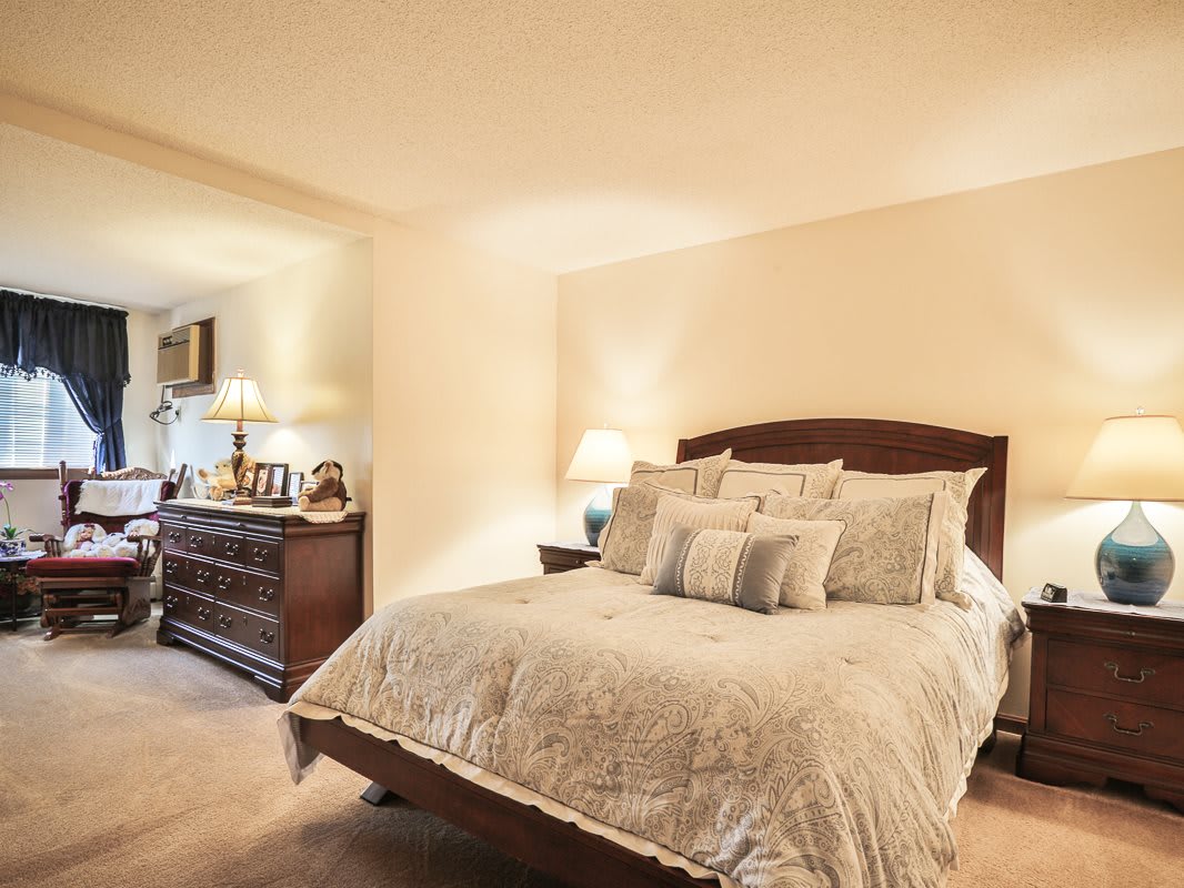 A cozy bedroom with a neatly made bed, elegant lamps, and polished furniture.