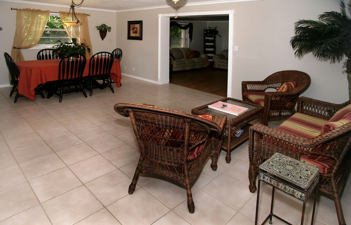 A cozy living room with wicker furniture and a dining area, featuring tile flooring and home decor.