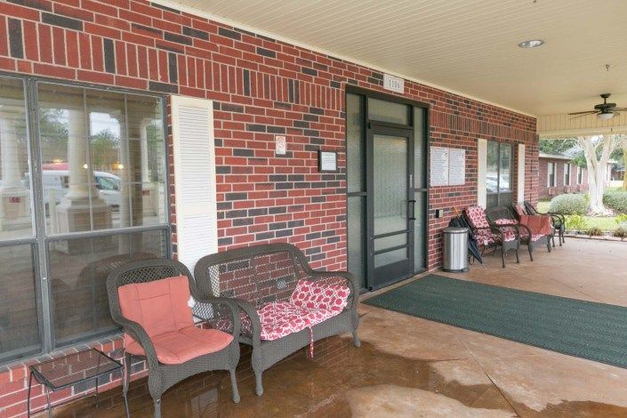 A cozy front porch with chairs and an entrance to a brick building.