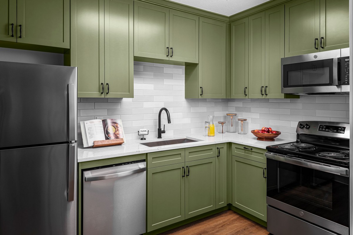 A modern kitchen with green cabinets and stainless steel appliances.