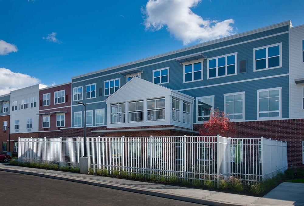 A modern residential apartment building with a white fence and a bright blue sky.