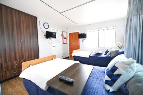 A cozy hotel room featuring two beds, a TV, and natural light from the window.
