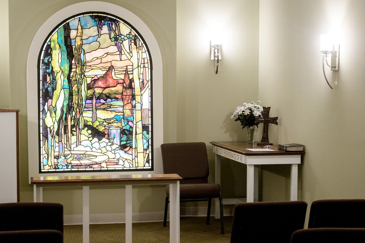 A serene chapel interior featuring a colorful stained glass window, a cross on a table, and arranged flowers.